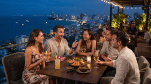 Photorealistic sophisticated nightlife travel photograph in Pattaya, Thailand, group of adult friends enjoying an outdoor rooftop bar overlooking the illuminated Pattaya coastline, elegant cocktails and Thai-inspired food on the table,