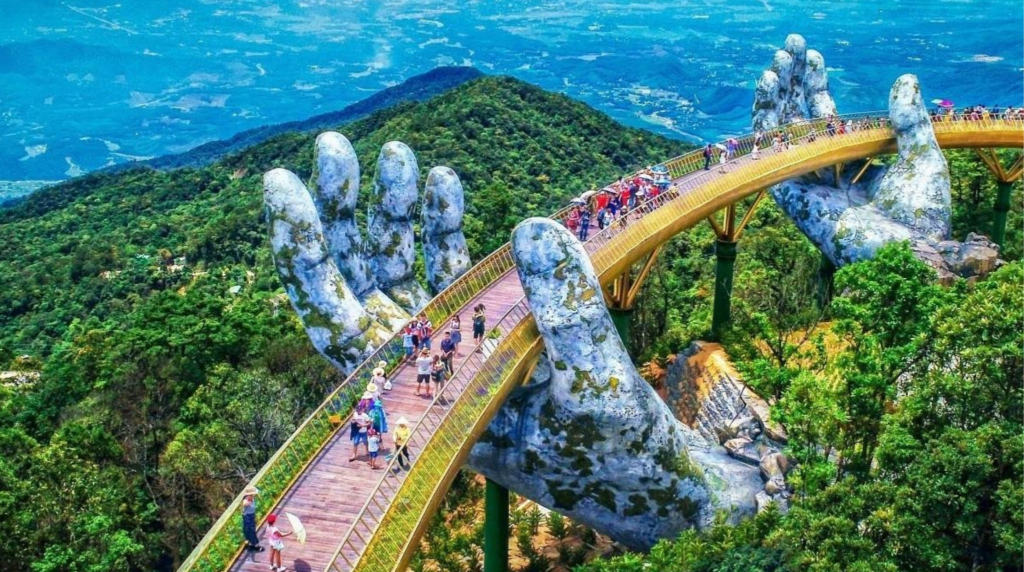 professional travel photograph of the Golden Bridge near Da Nang, Vietnam, famous pedestrian bridge supported by enormous weathered stone hands rising from lush green mountain vegetation,