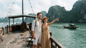 professional lifestyle travel photograph aboard a traditional Vietnamese Halong Bay cruise, real adult couple standing naturally on the wooden upper deck looking at limestone karst islands