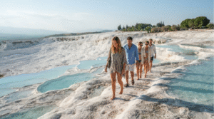 l lifestyle photograph of adult travellers walking carefully across the white Pamukkale travertine terraces in Turkey, shallow turquoise thermal pools surrounding them, dramatic white limestone landscape