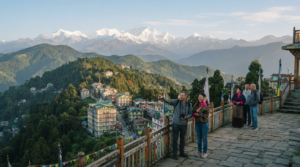 travel photograph of Pelling, Sikkim, showing a peaceful Himalayan town surrounded by lush green slopes with dramatic snow-covered mountain peaks visible in the distance