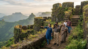 travel photograph of random diverse Indian tourists exploring a historic Maratha hill fort in Maharashtra, weathered stone walls, dramatic Western Ghats landscape and green