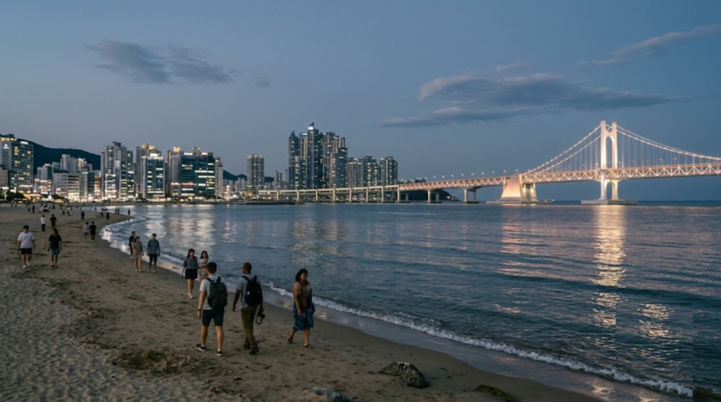 travel photograph of Gwangalli Beach in Busan, South Korea, wide sandy coastline with illuminated Gwangan Bridge stretching across the bay