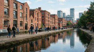Manchester canal district, historic brick buildings beside a calm canal, modern city architecture in the background, diverse random tourists walking along the waterfront
